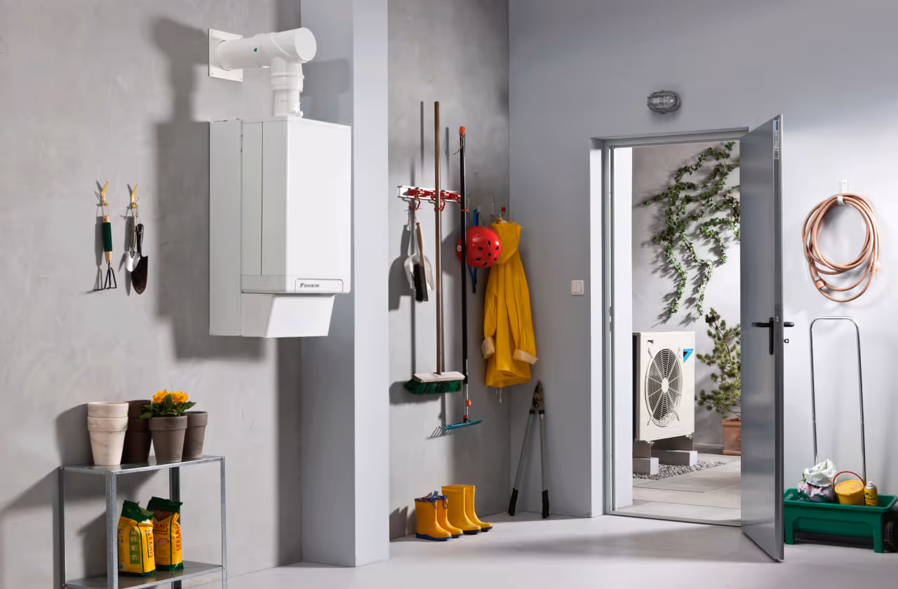Utility room with wall-mounted heating unit, gardening tools, boots, and open door to outdoor space.