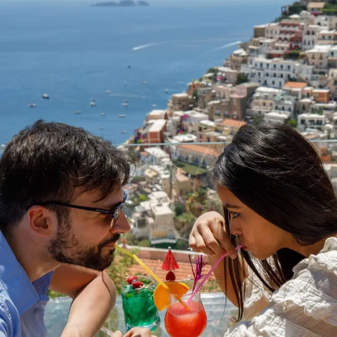 Couple sipping cocktails on a balcony overlooking the sea and boats near Positano