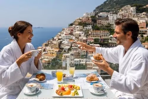 Couple in white robes enjoying breakfast with coffee and croissants overlooking Positano