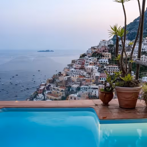 Infinity pool overlooking Positano with boats scattered in the bay at dusk