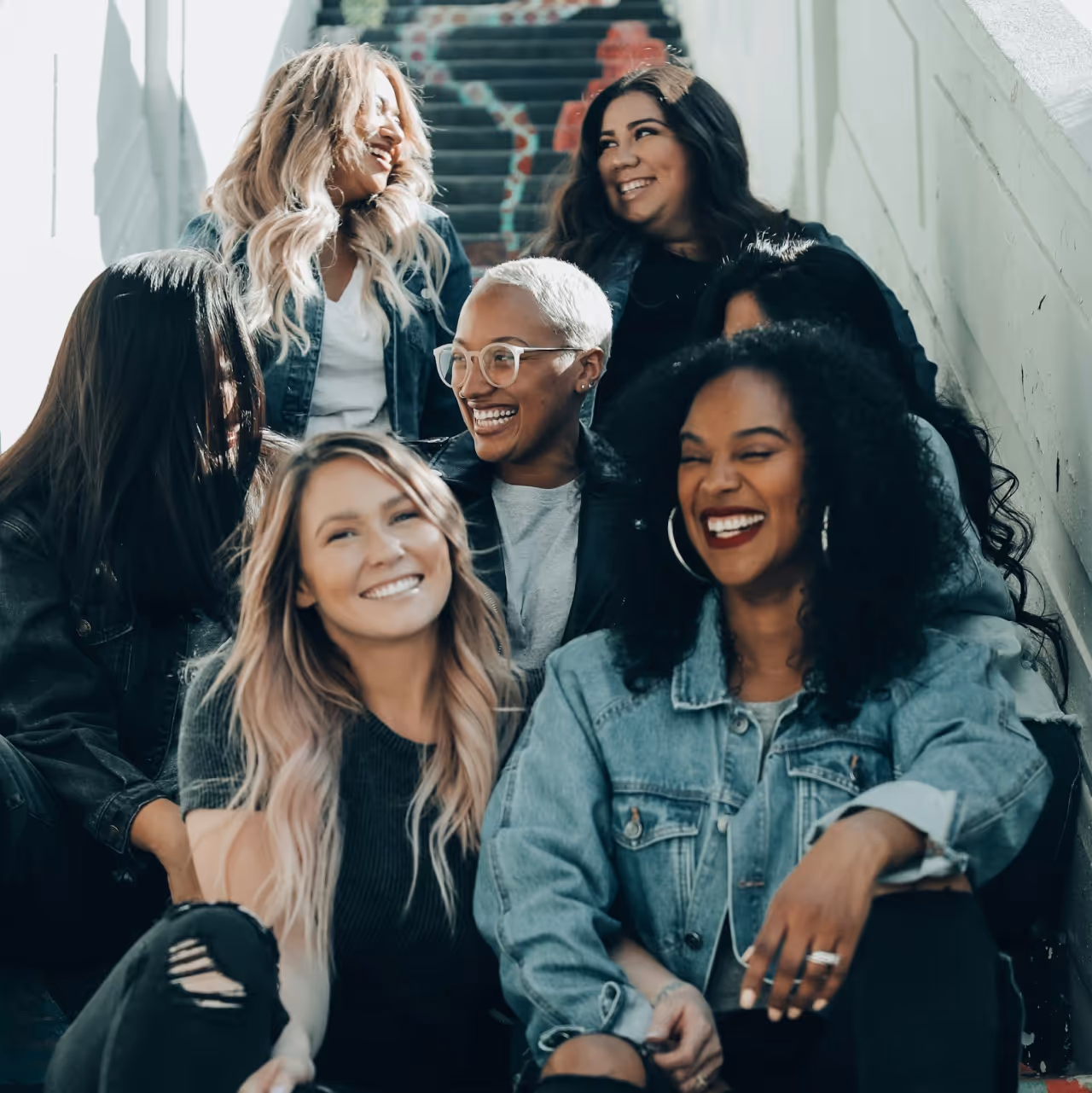 un groupe de femmes assises dans un escalier, face caméra, en train de sourire et de passer un bon moment