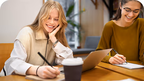 Deux femmes travaillant sur ordinateur et prenant des notes dans un espace de coworking convivial.