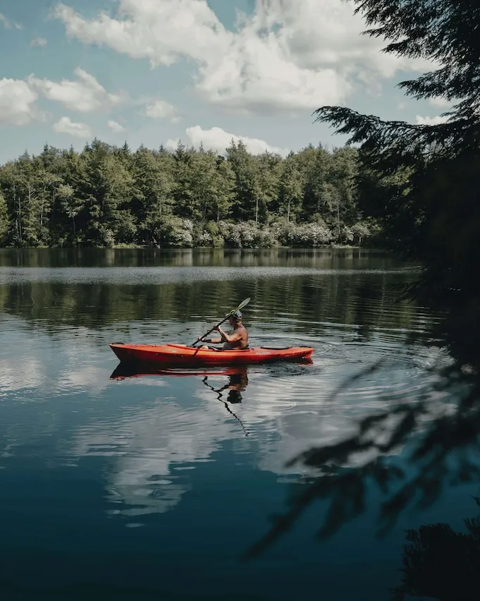 Man kayaking on a lake wearing no shirt and a cap.