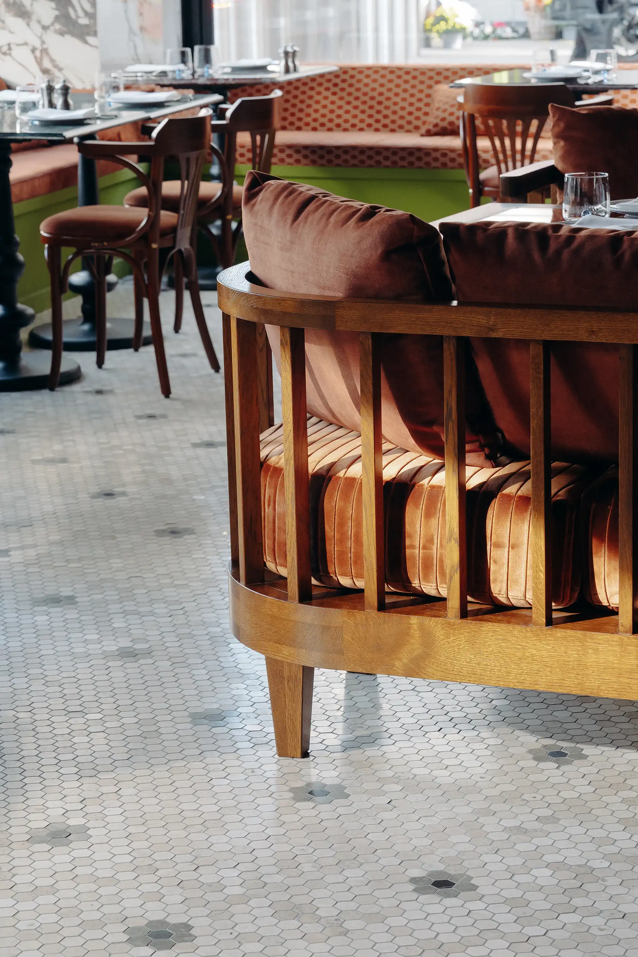 Cozy restaurant interior with wooden-framed seating featuring rust-colored cushions and hexagonal tile flooring with scattered darker hexagonal accents.