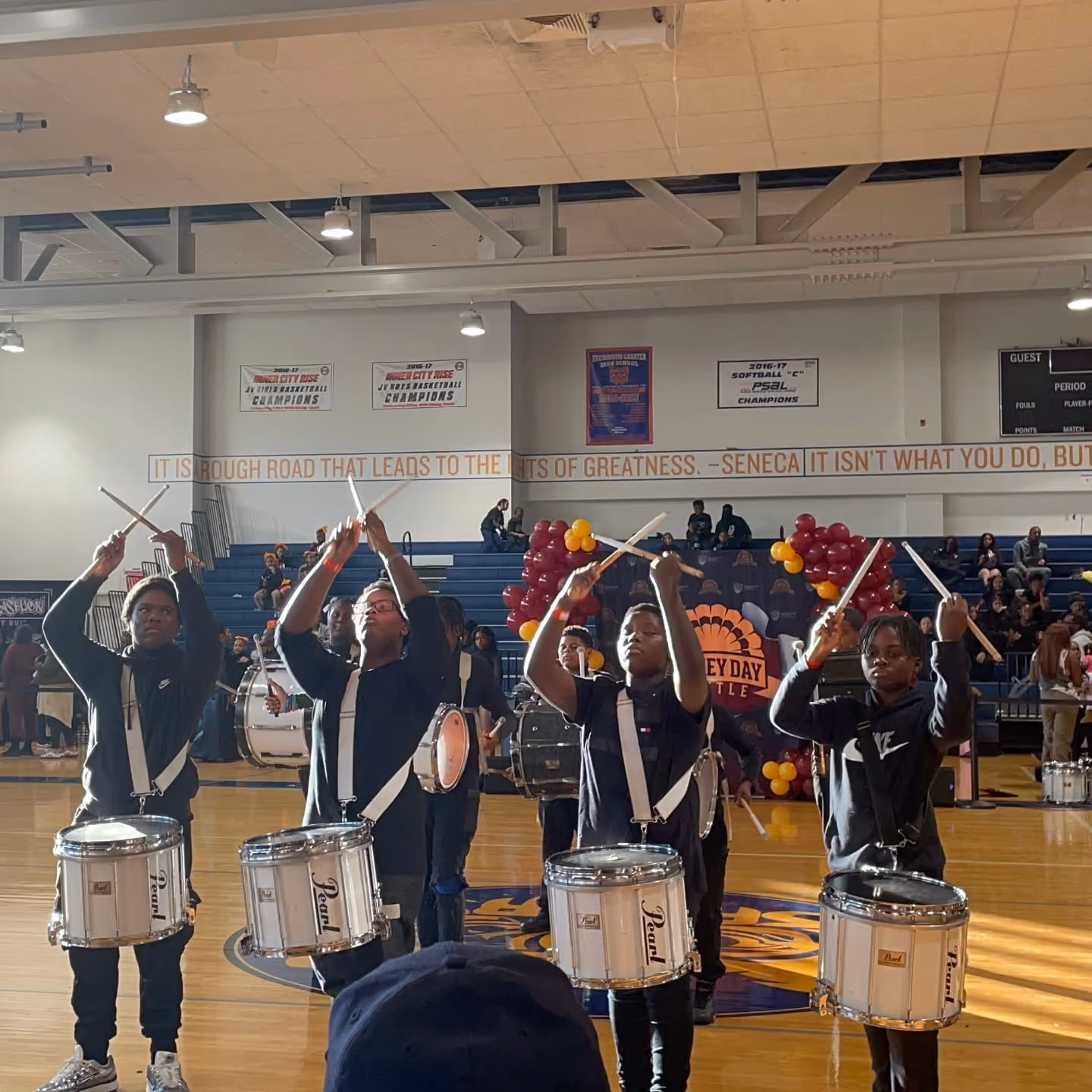 Student drumline performing with snare drums in school gymnasium