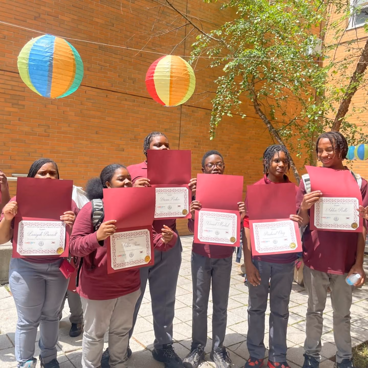 Students in uniforms proudly displaying award certificates outdoors