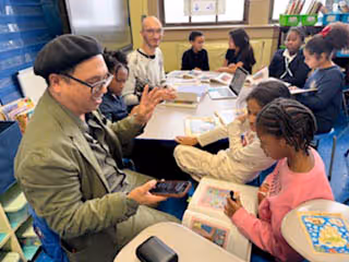 Teacher engaging with elementary students in a classroom around a table with books and a tablet.