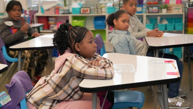 Children sitting at desks in a classroom, attentively looking forward.