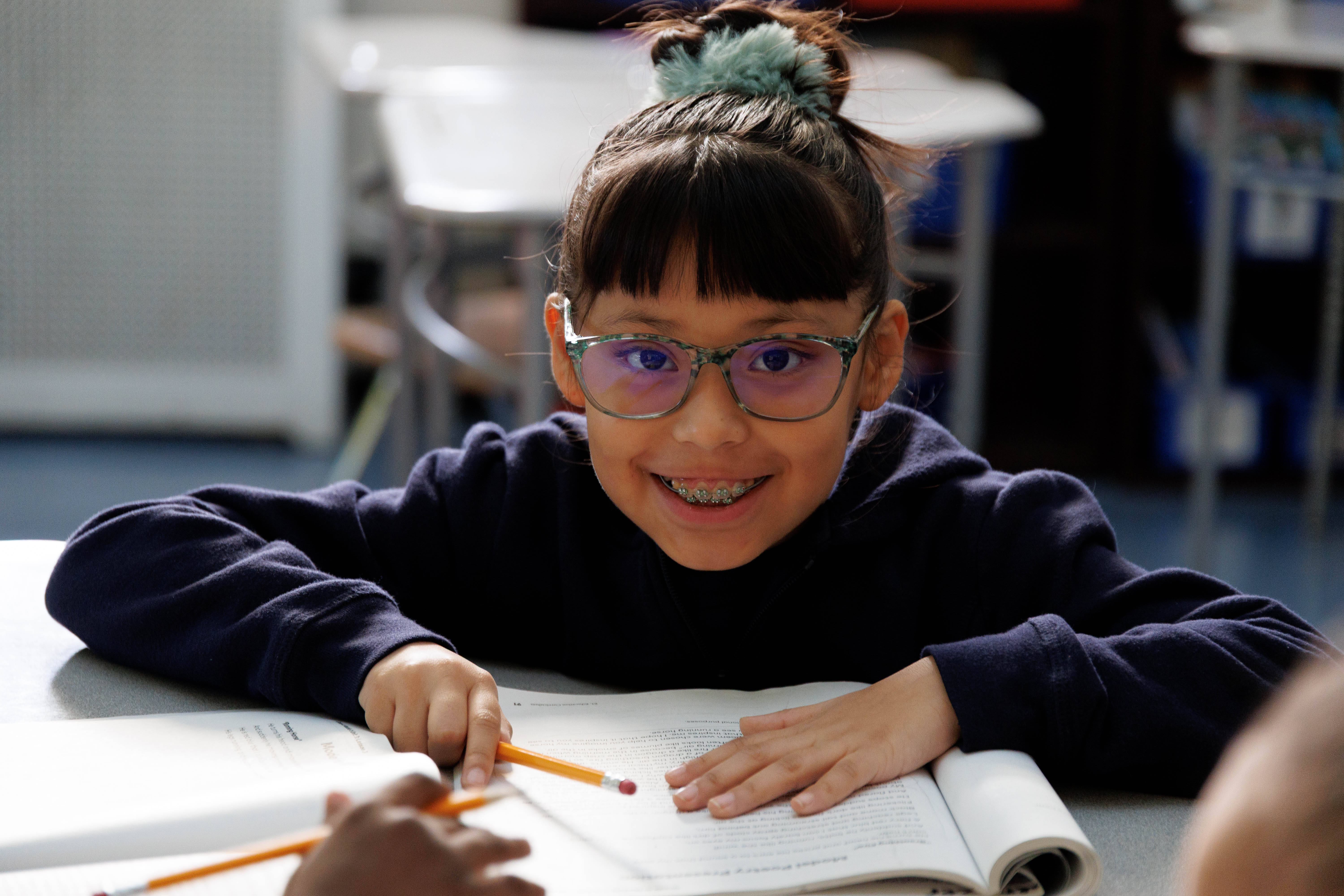 Smiling student with glasses reads at classroom desk