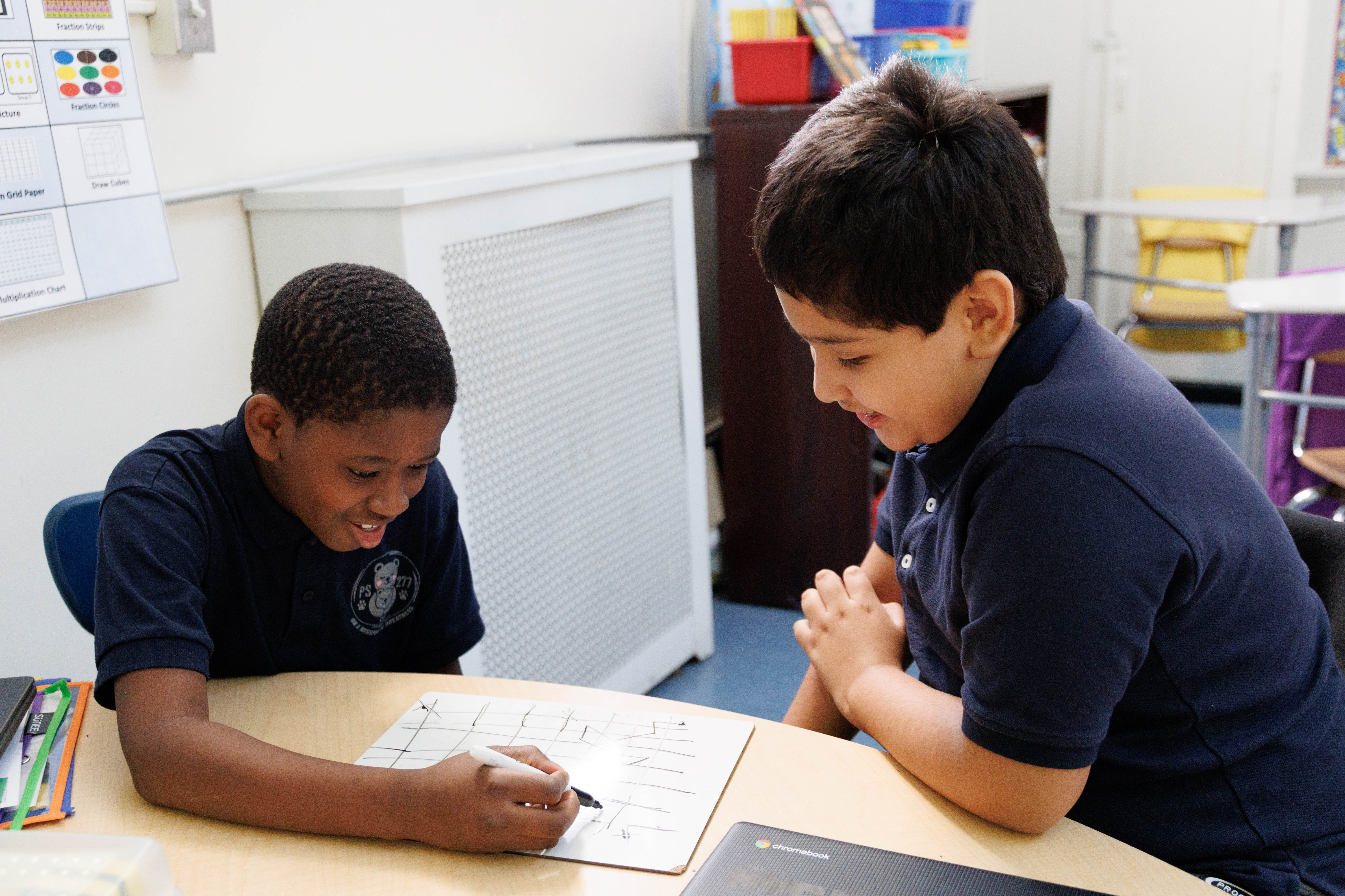Two students in uniform collaborating on a whiteboard math activity