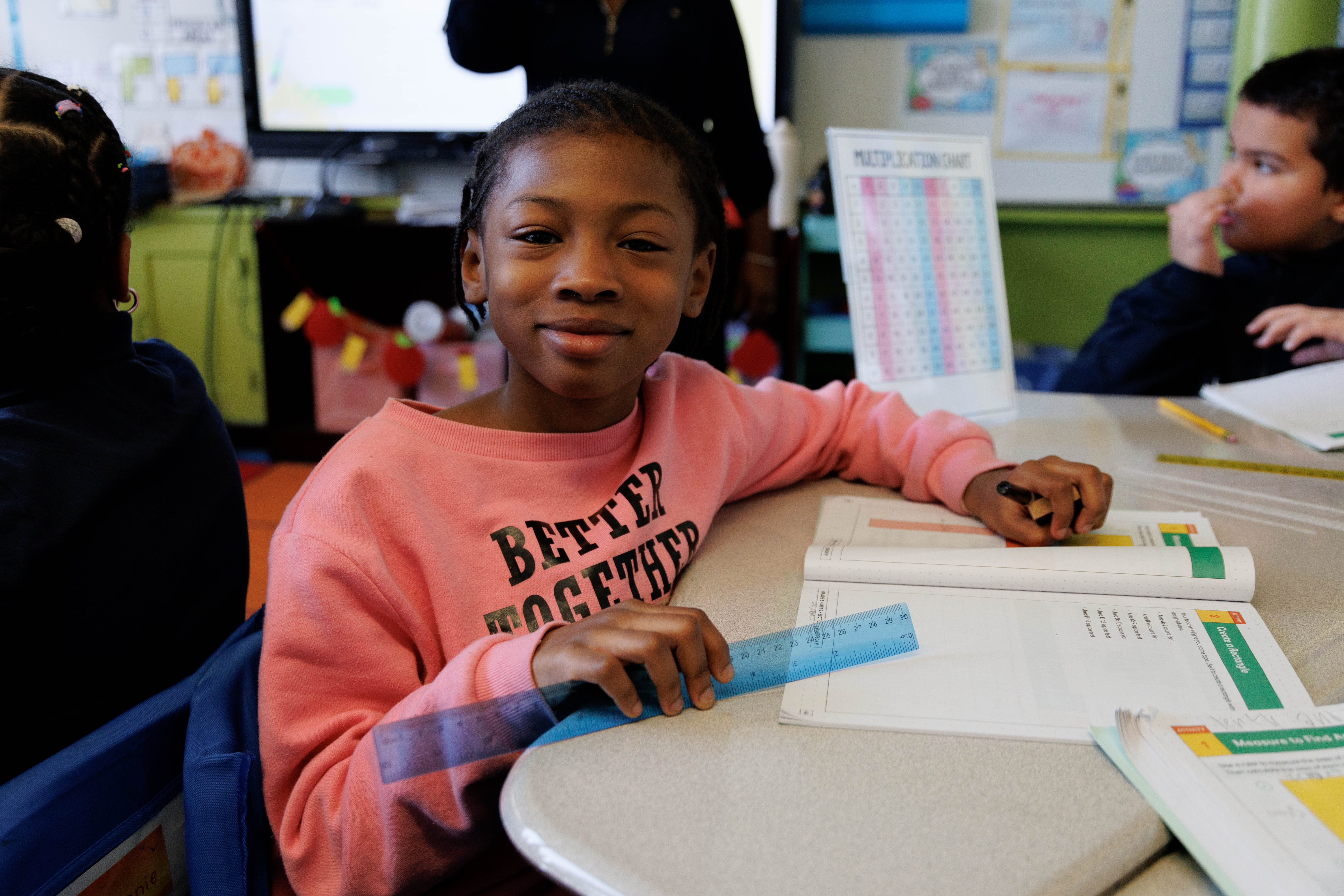 Student smiling at desk with ruler and math workbook
