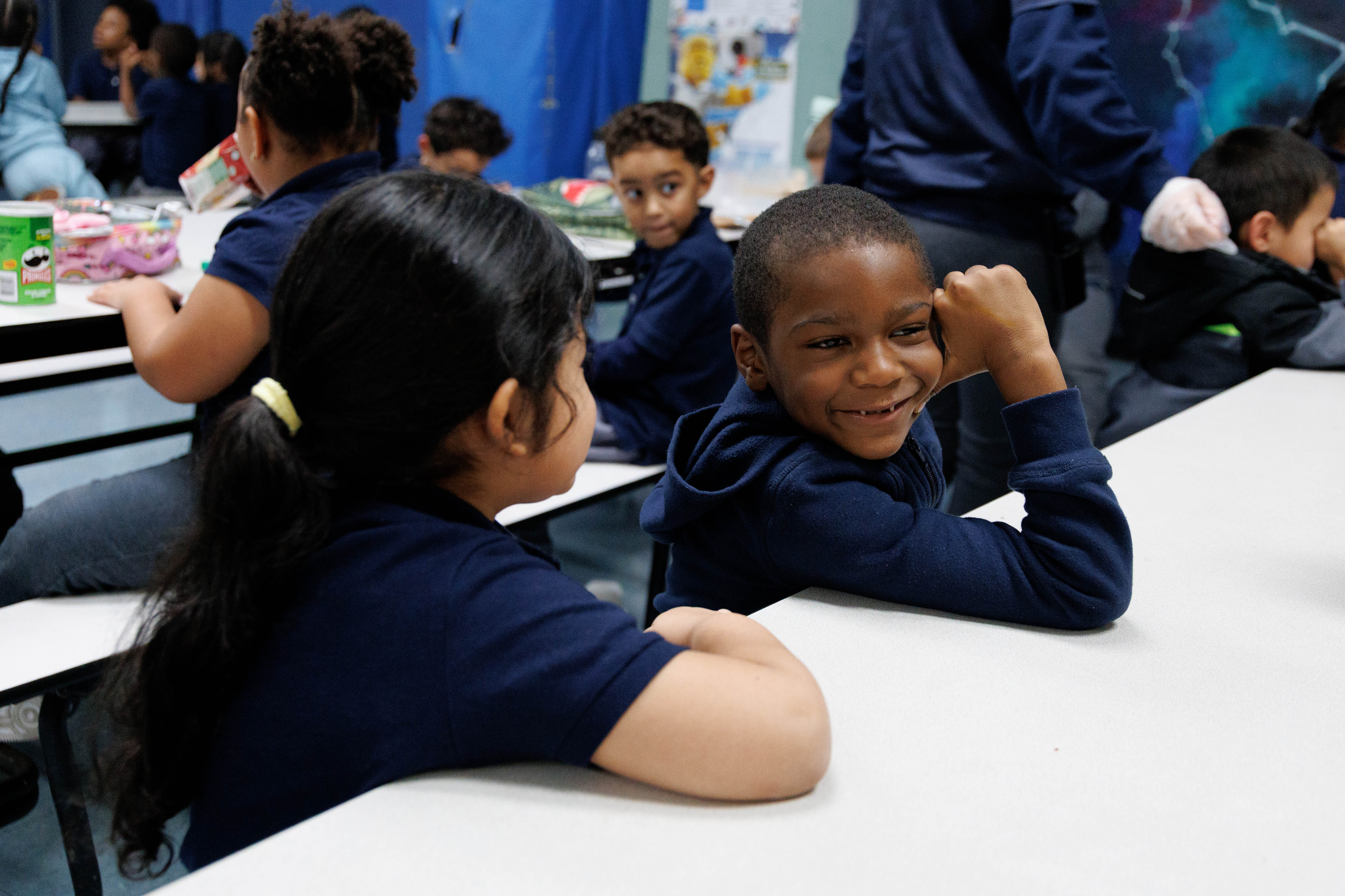 Smiling elementary student in uniform chatting with classmate at cafeteria table