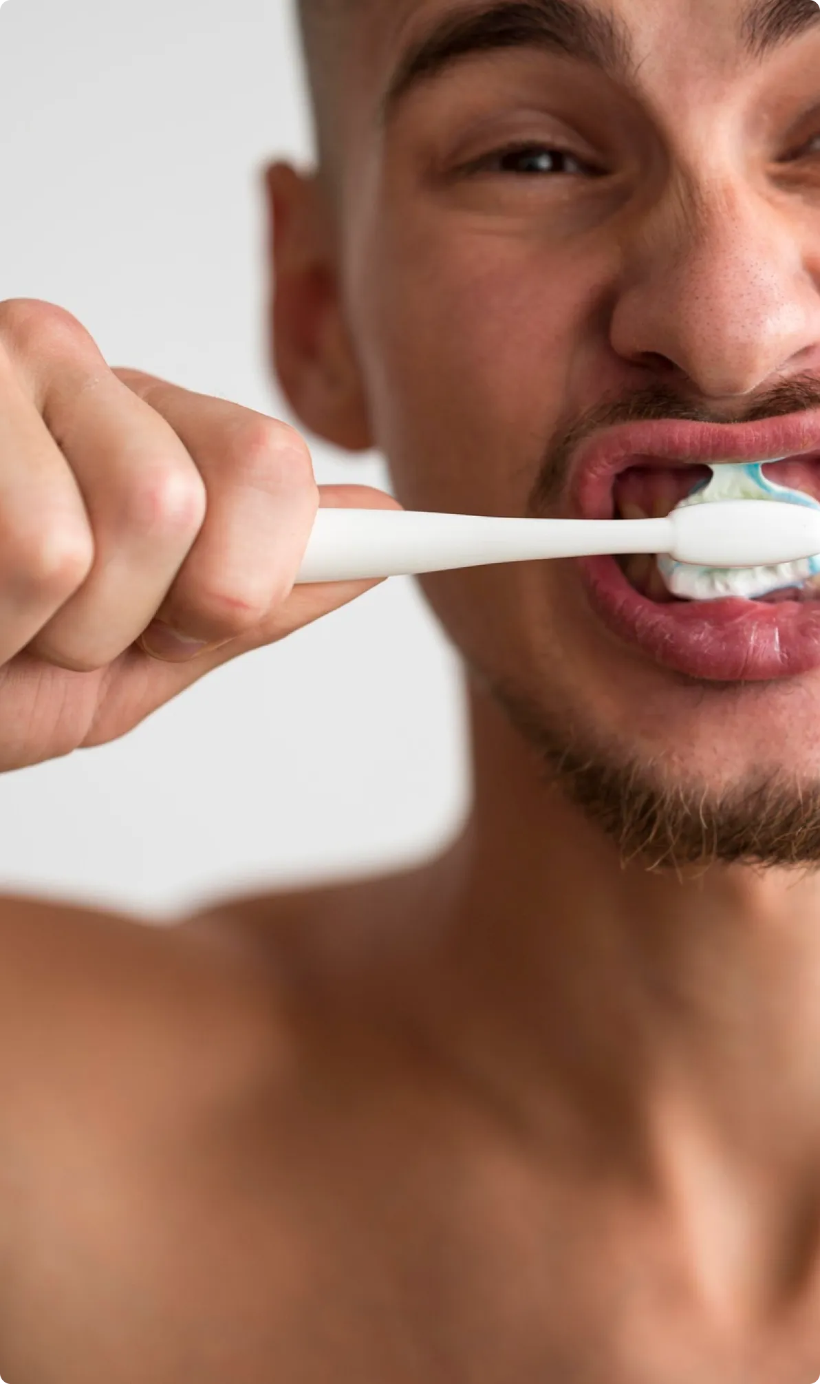 Close-up of a man brushing his teeth with a white toothbrush and toothpaste foam.