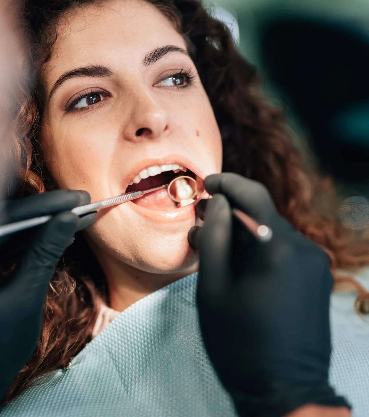 Dentist wearing black gloves examining a patient's teeth using dental mirror and probe.