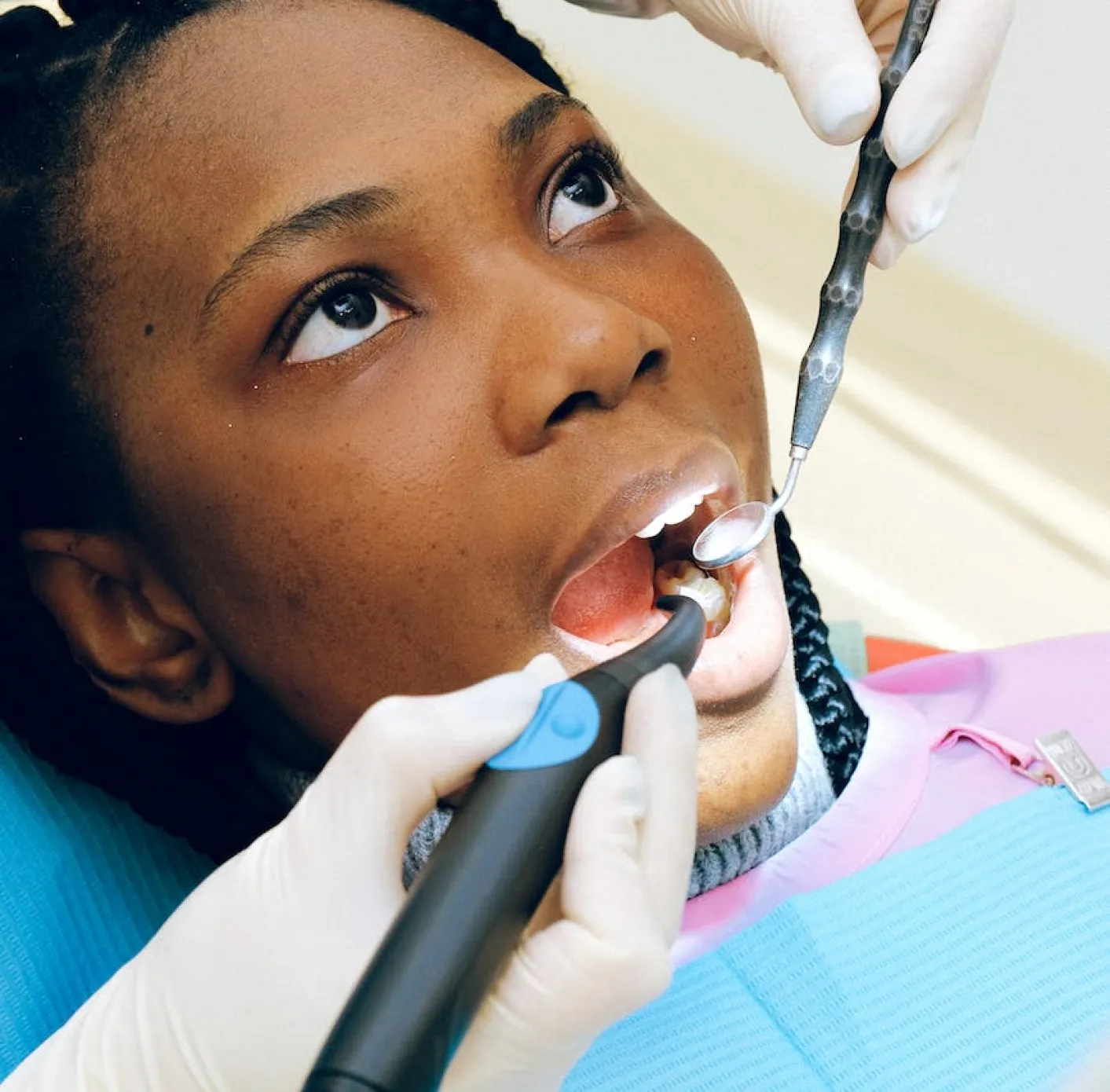 Dentist wearing white gloves examining a patient's open mouth with dental tools.