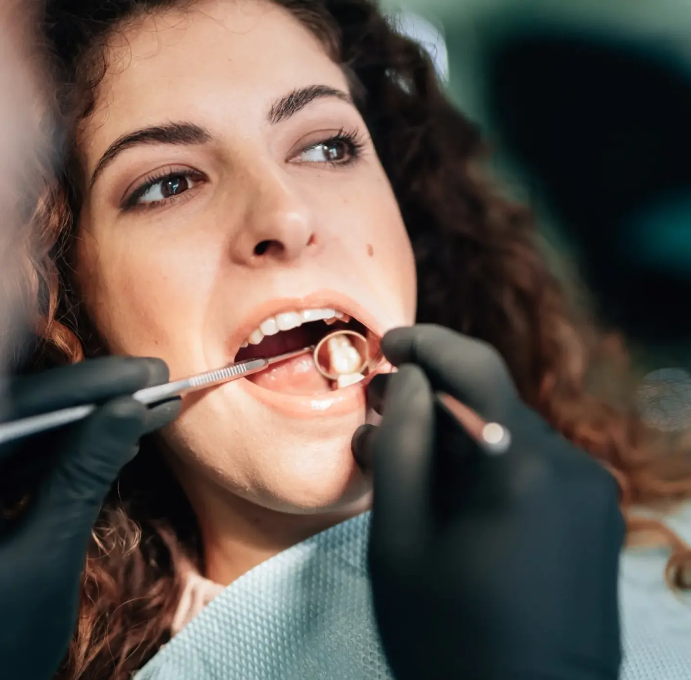 Close-up of a woman receiving a dental checkup with a dental mirror and probe inside her mouth.