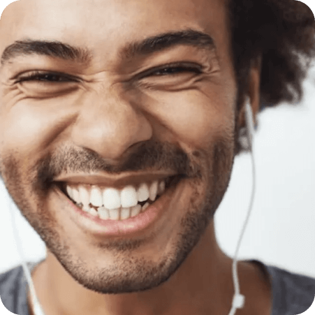 Close-up of a man smiling broadly while wearing white earphones.