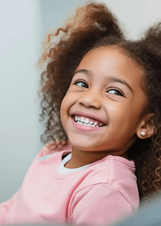 Happy young girl with curly hair smiling and looking to the side wearing a pink shirt.