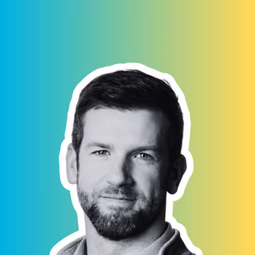 Close-up portrait of a bearded man with short dark hair against a blue to yellow gradient background.