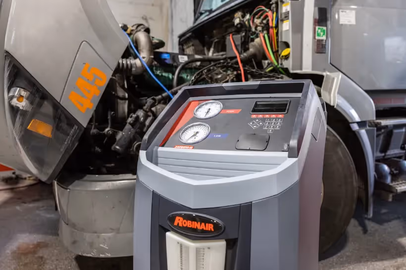 HVAC improve for winter service using a Robinair unit beside an open semi truck with visible engine components.