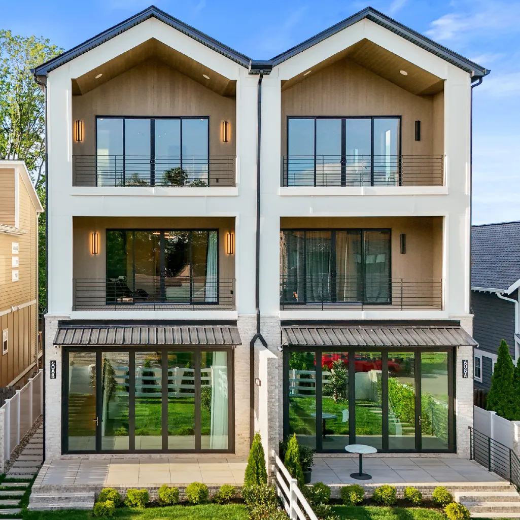 Modern twin townhouses with large glass windows, balconies, and small front yards separated by a white fence.