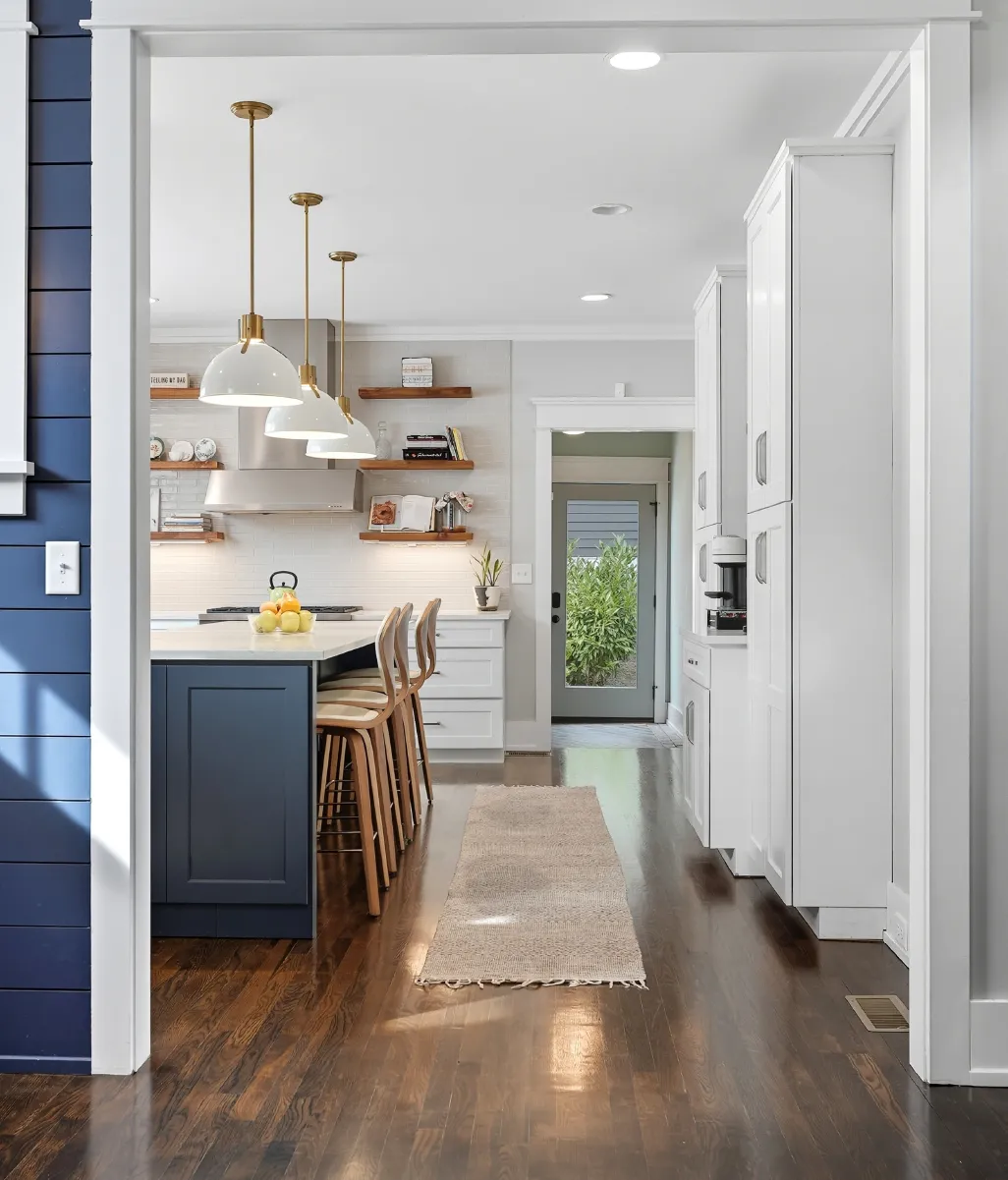 Modern kitchen with dark hardwood floors, blue island with wooden stools, pendant lights, white cabinetry, and a back door with glass panel.