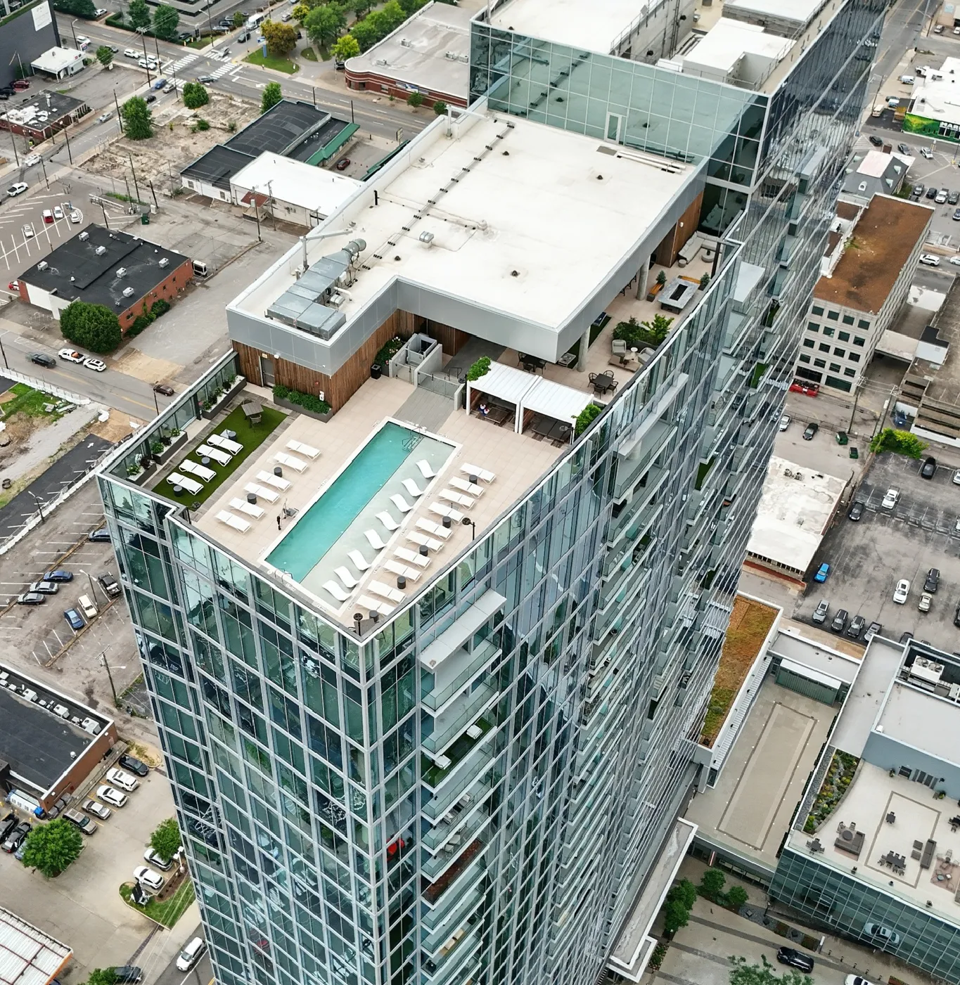Aerial view of a modern high-rise building with a rooftop pool surrounded by lounge chairs and outdoor seating.