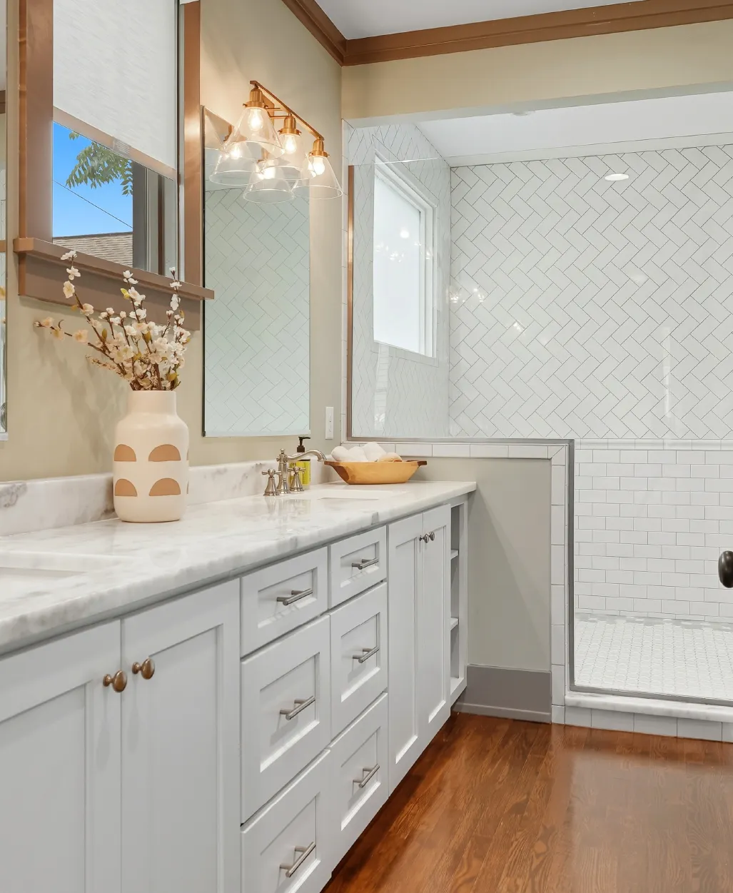 Modern bathroom with white cabinetry, marble countertop, large mirror, flower vase, and tiled walk-in shower.