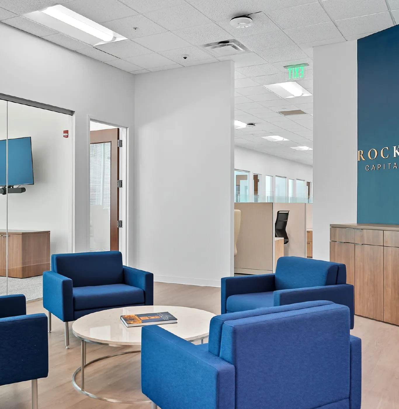 Modern office lounge area with four blue armchairs around a round white marble table with a book on it.