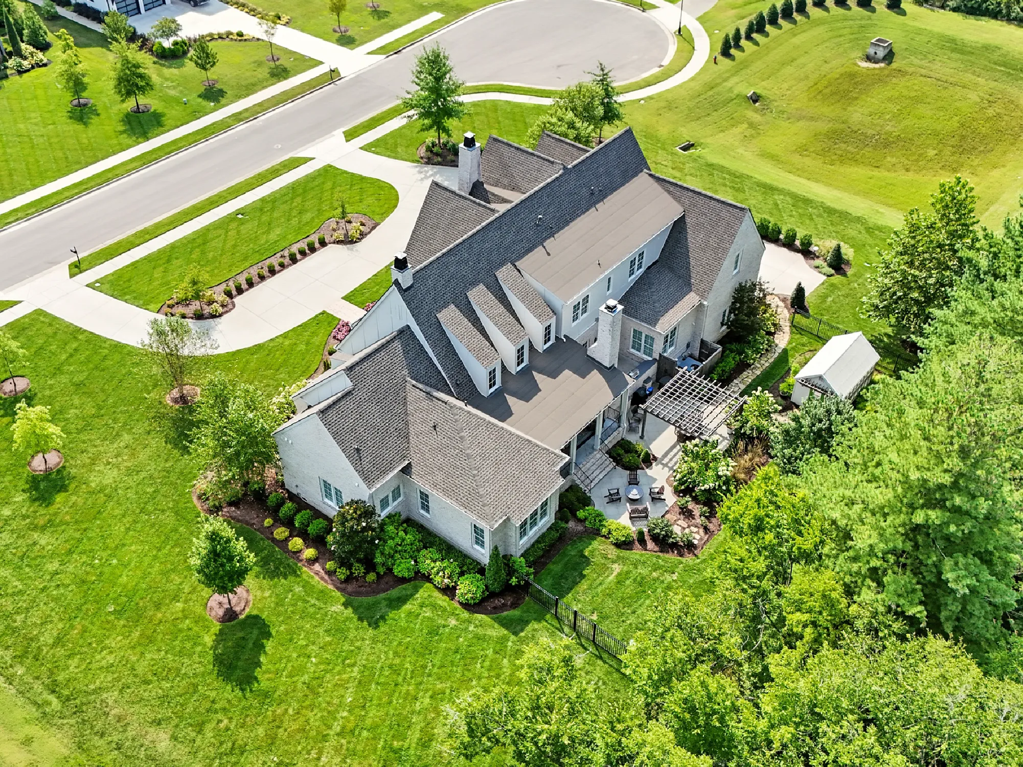 Aerial view of a large house with multiple gabled roofs surrounded by well-maintained green lawns, trees, and landscaped gardens.