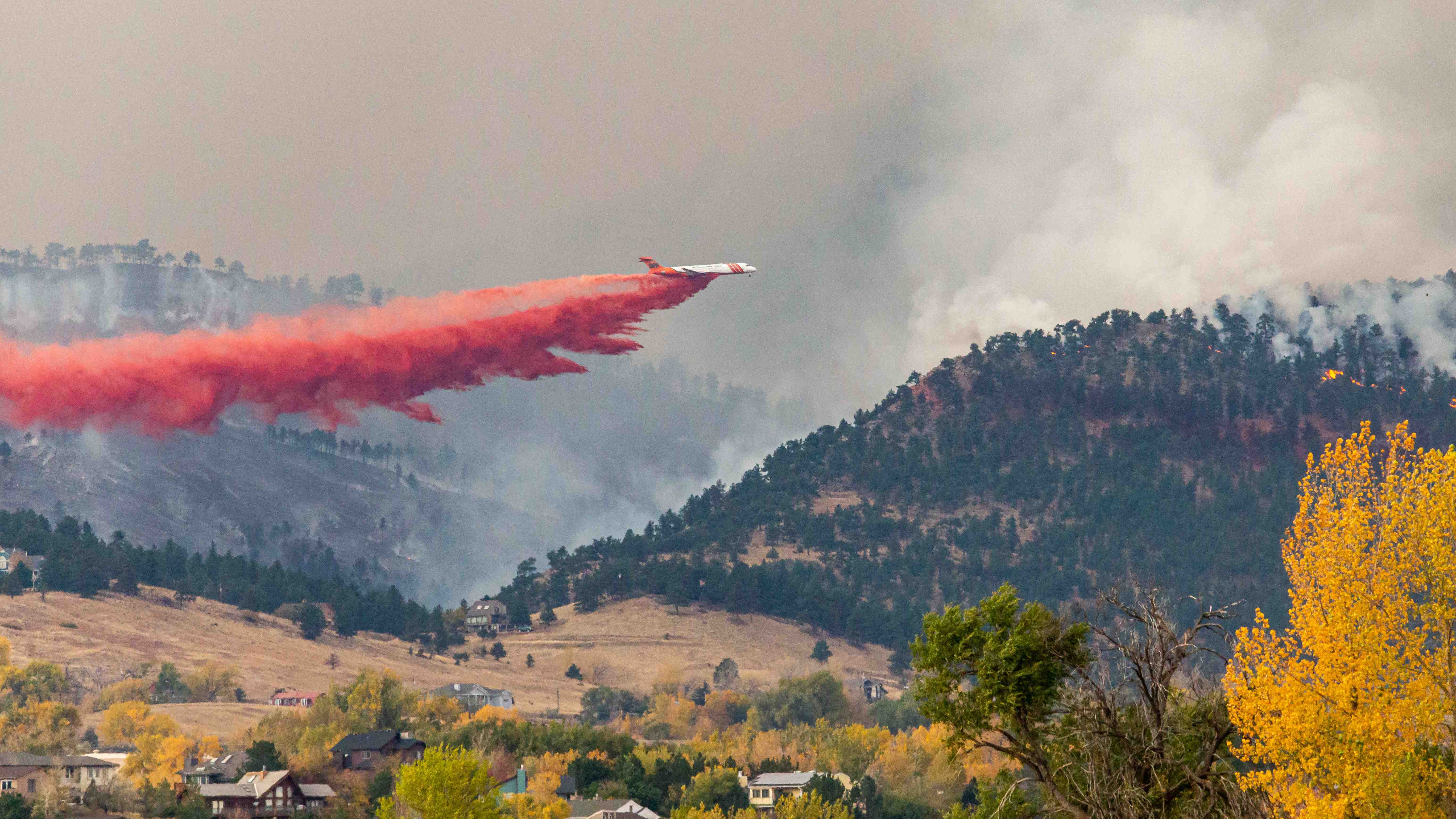 VLAT doing retardant drop along fireline with homes in foreground 