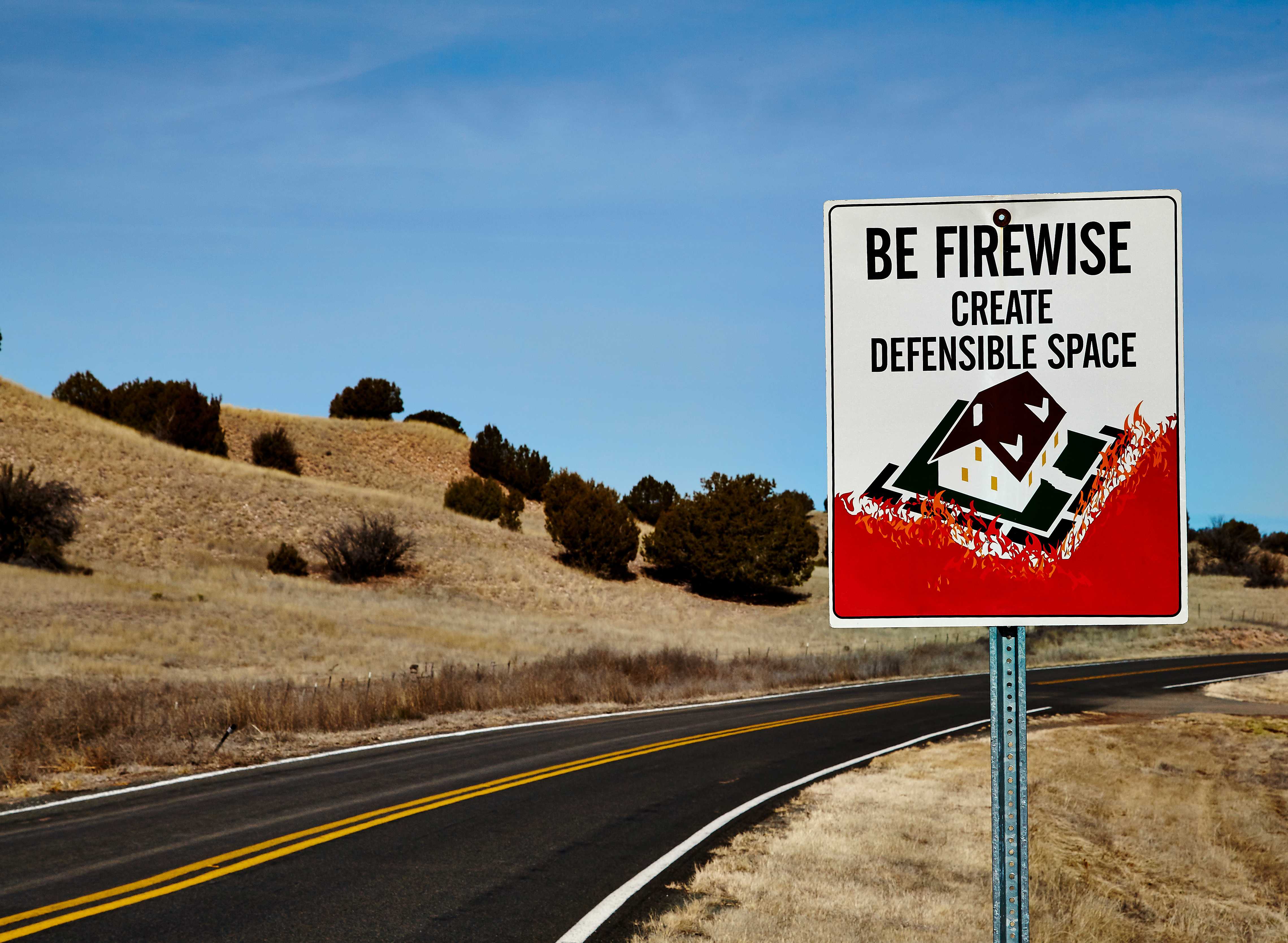 "Be firewise, create defensible space" sign along a roadway surrounded by highly flammable dried grass