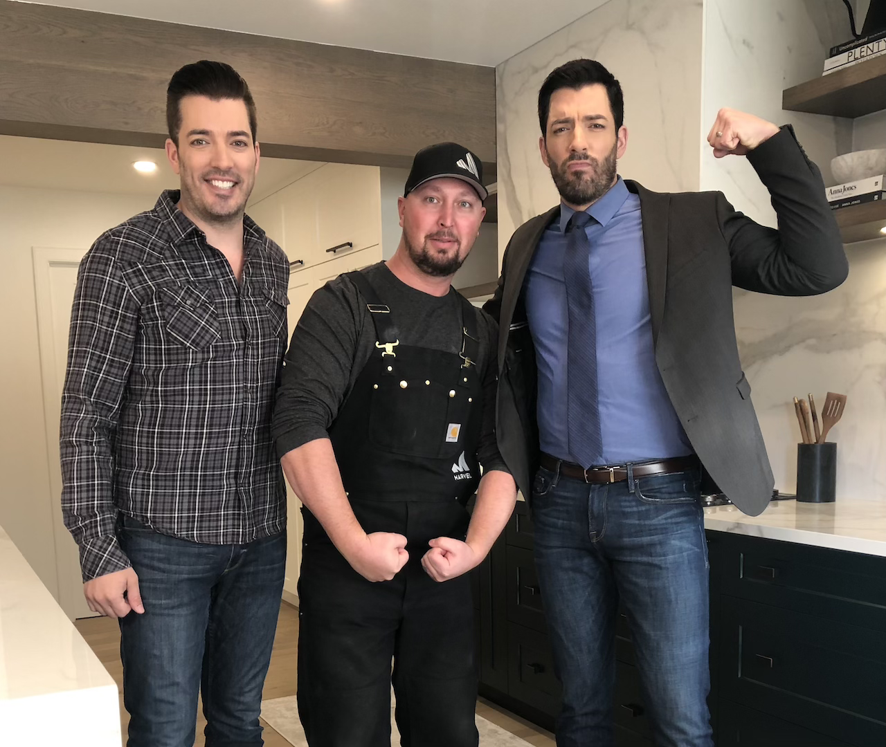 Three men standing in a modern kitchen during a shoot for HGTV's The Property Brothers Celebrity I.O.U with Marvel Cabinetry.