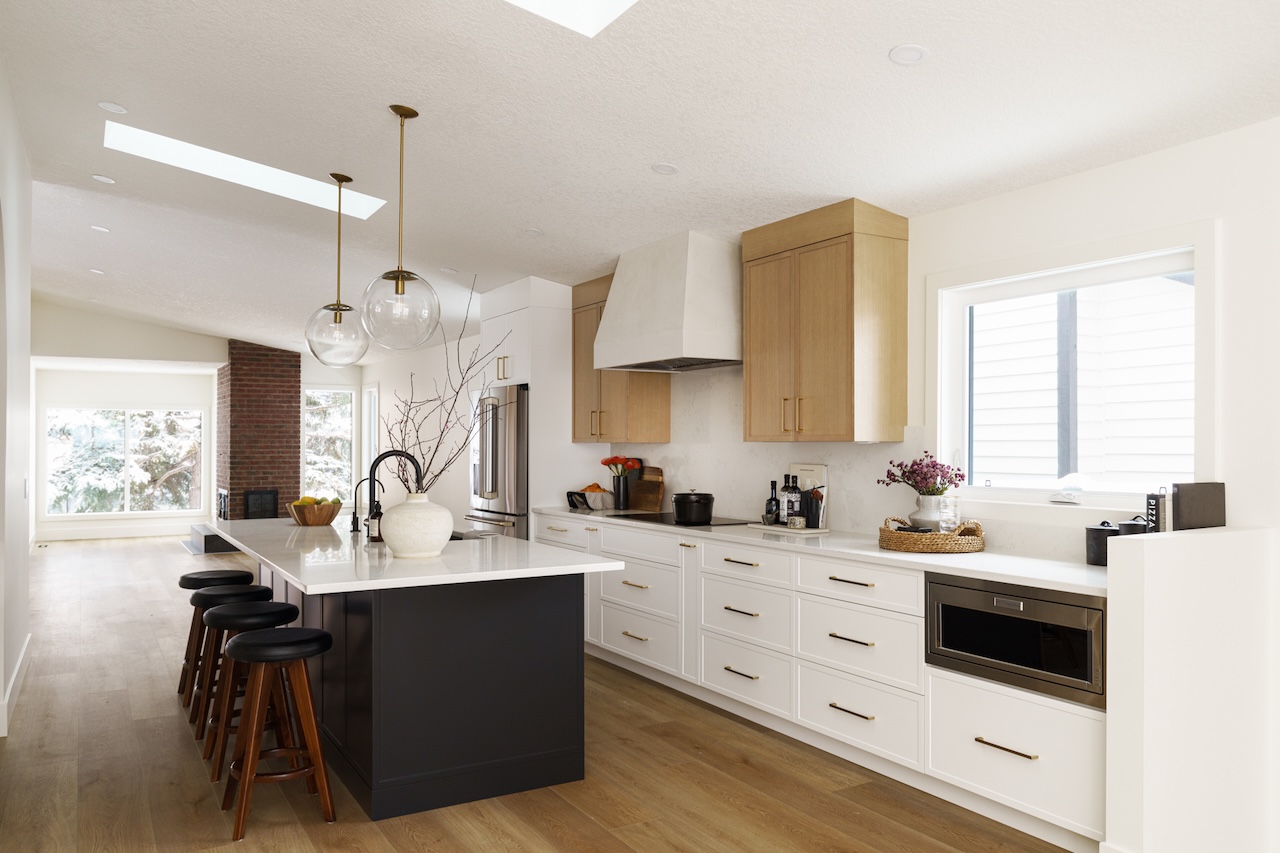 Bright modern kitchen with large island, four wooden stools, white countertops, light wood cabinets, and pendant lights by Marvel Cabinetry.