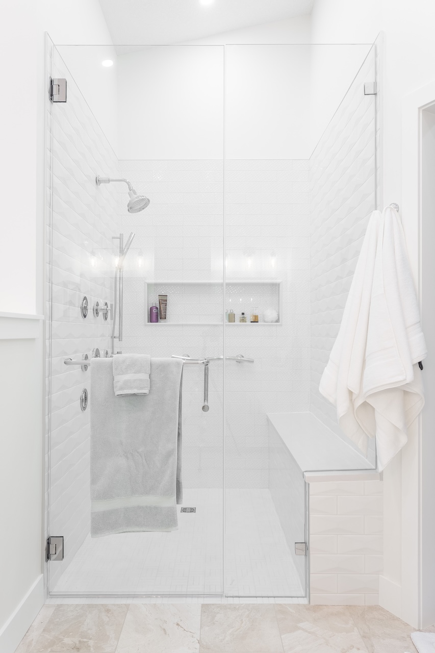 Modern living room with light blue armchairs, a small black side table, a brown chair, and a built-in wine rack filled with bottles against a white wall with black framed glass doors nearby by Marvel Cabinetry.