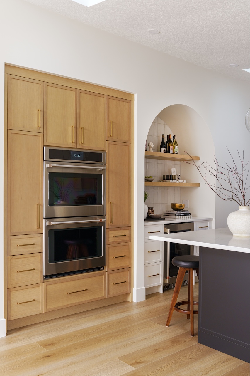 Bright modern kitchen with large island, four wooden stools, white countertops, light wood cabinets, and pendant lights by Marvel Cabinetry.