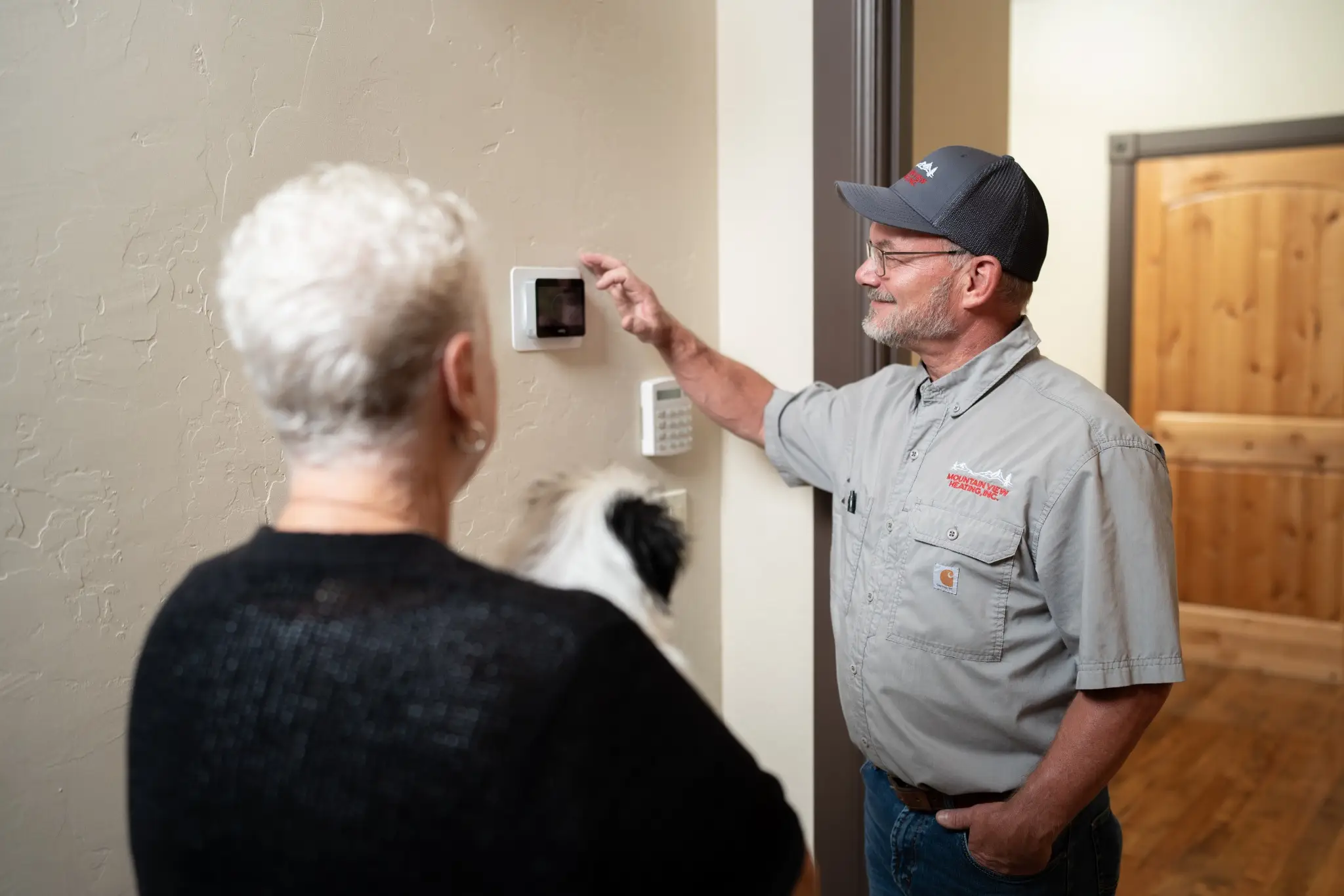 HVAC technician adjusting a wall thermostat for an elderly homeowner.