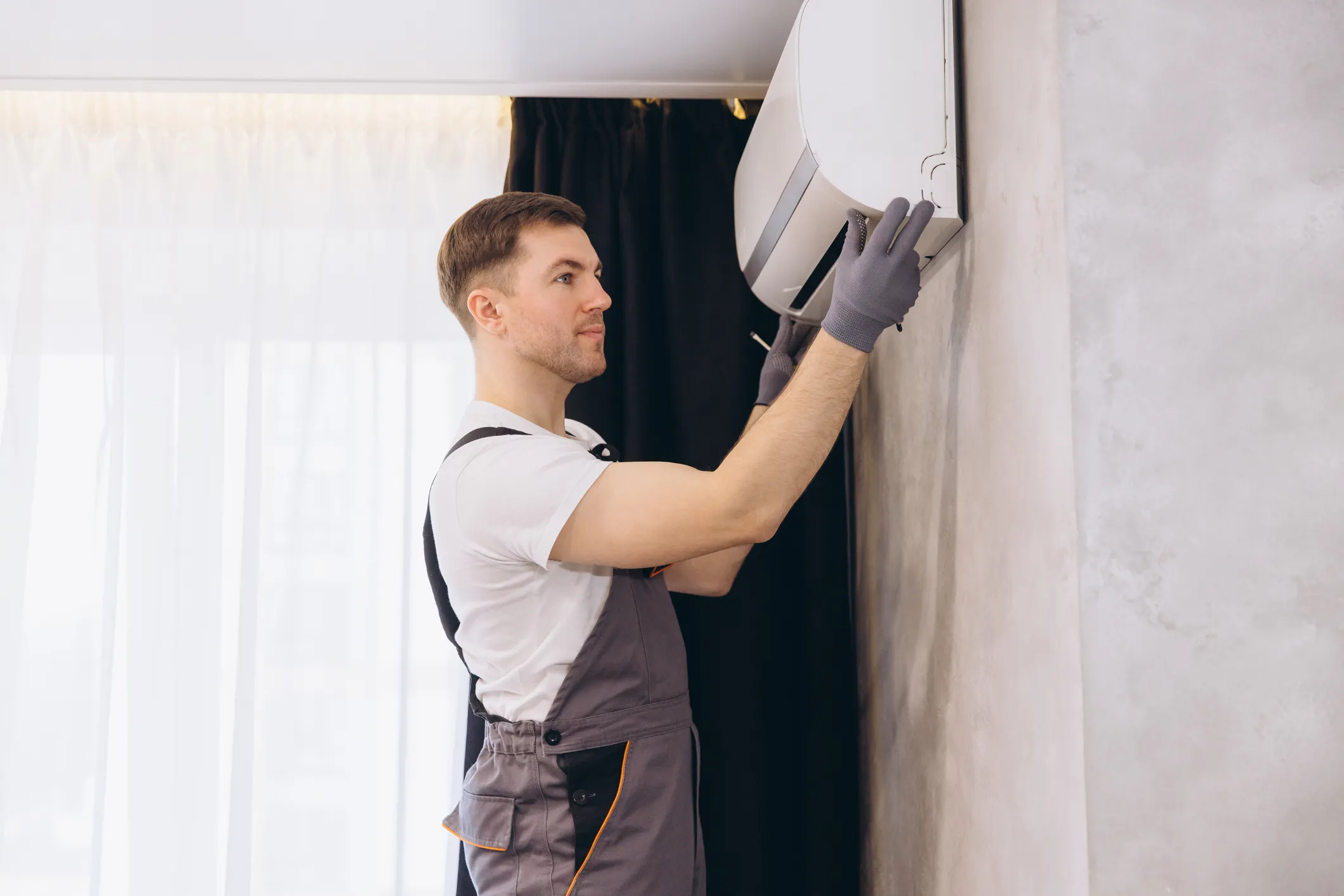 An HVAC technician installing an indoor air conditioning unit on a wall.