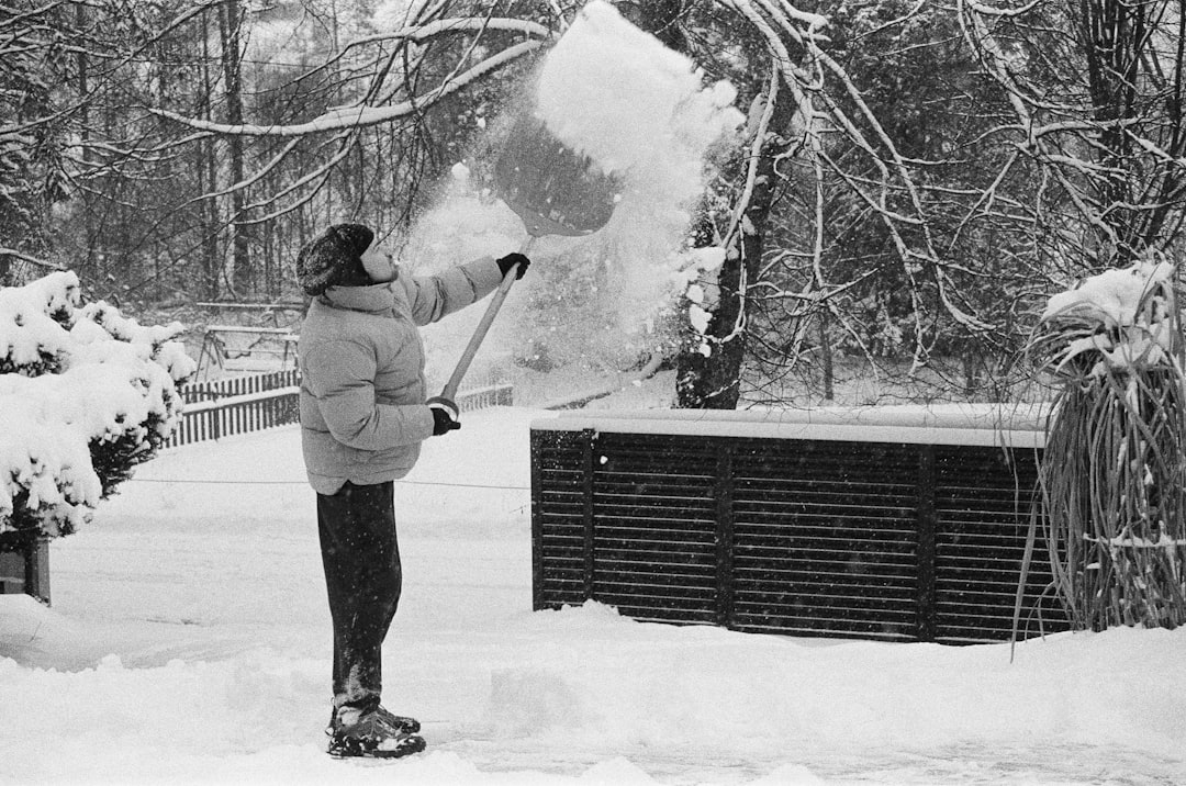 Technician clearing snow and ice away from a residential heat pump outdoor unit