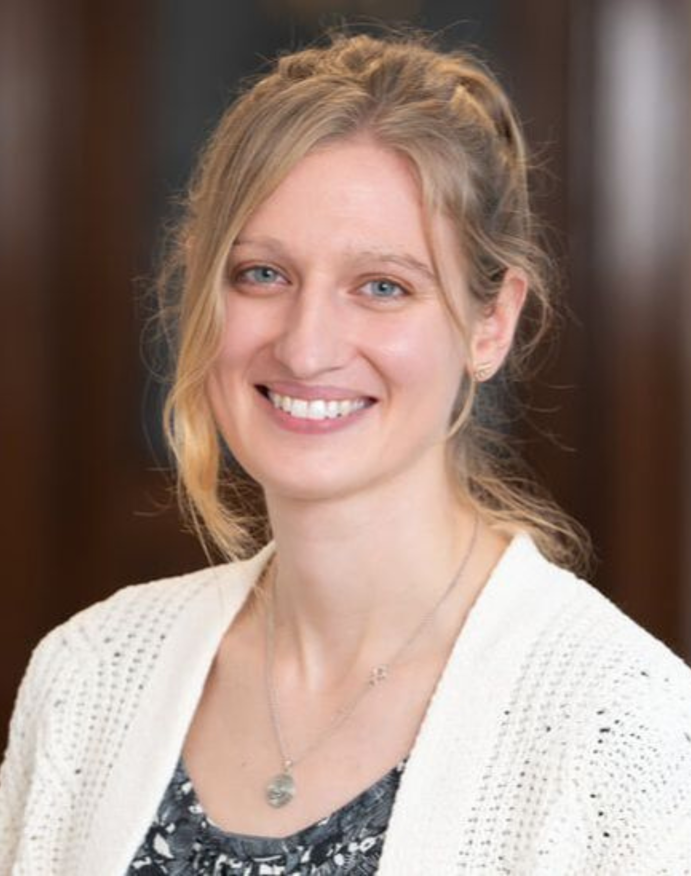Hope Wall - smiling woman with blonde hair tied back, wearing a white knitted cardigan and a necklace.