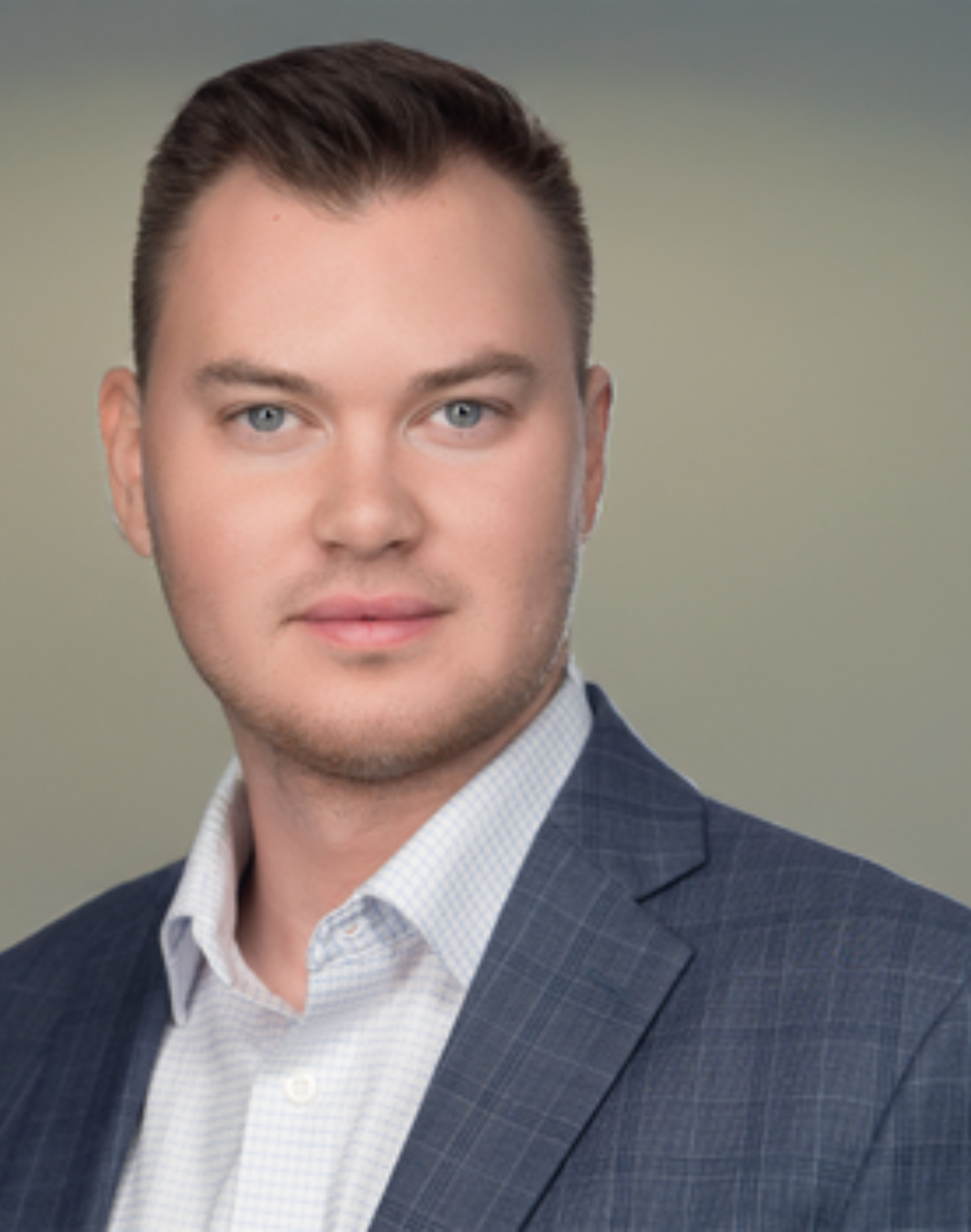 Ty;er St. Marie - Headshot of a man with short brown hair wearing a blue checkered blazer and a white checkered shirt against a neutral gradient background.