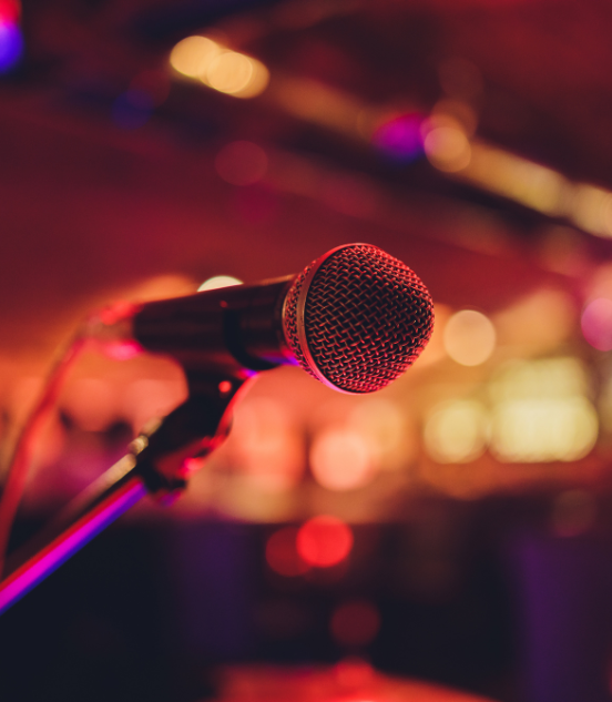 Close-up of a microphone on a stand with colorful blurred lights in the background, suggesting a performance or karaoke setting.