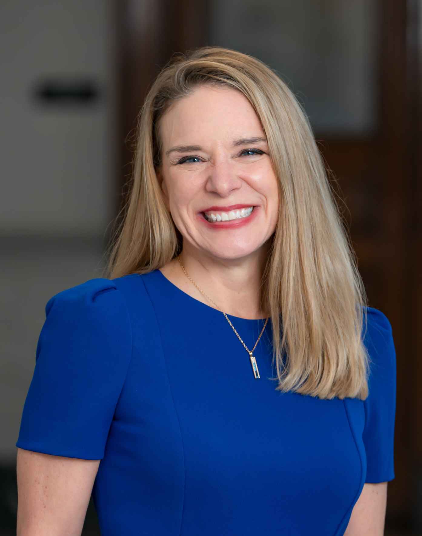 Summer Nitsch - smiling woman with long blonde hair wearing a royal blue dress and a gold necklace.