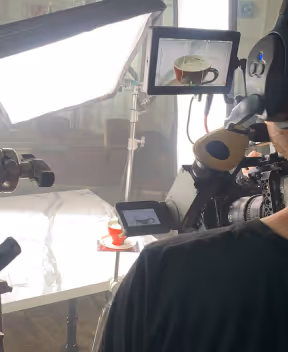 Camera setup filming a red cup on a table, with studio lights and monitors showing the cup.