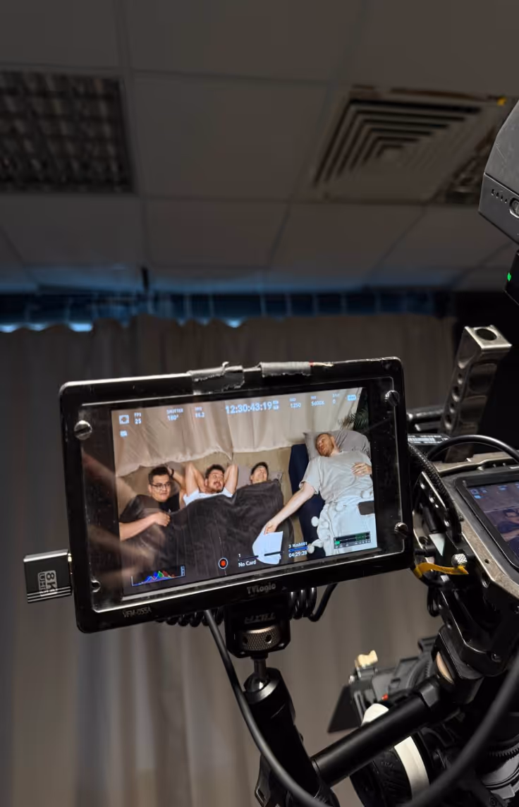 Camera monitor shows four men lying on a bed covered with a black blanket inside a room.