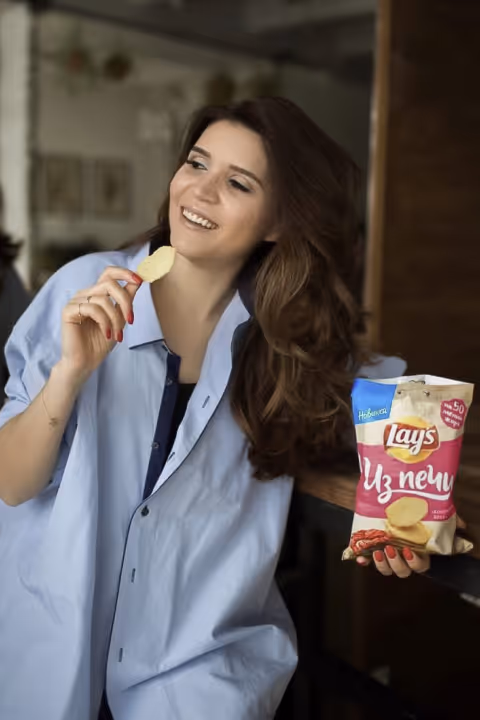 Woman in blue shirt smiling while holding a chip and a bag of Lay's chips.