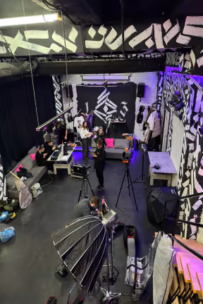 Studio space with black and white abstract wall art, people interacting, and photography equipment.