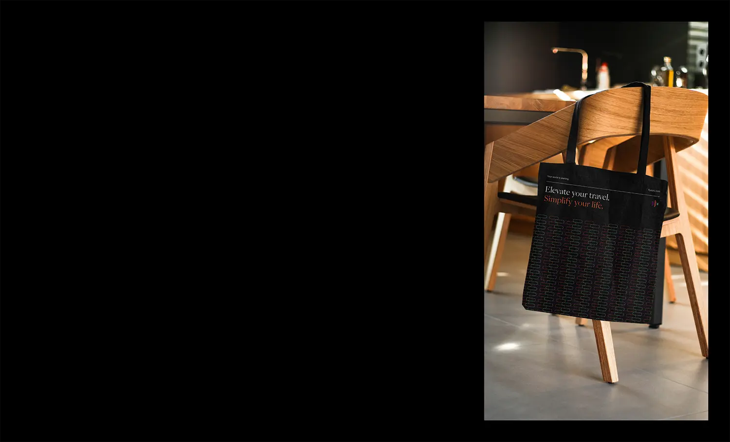 Black tote bag with travel brand tagline printed in elegant serif type.