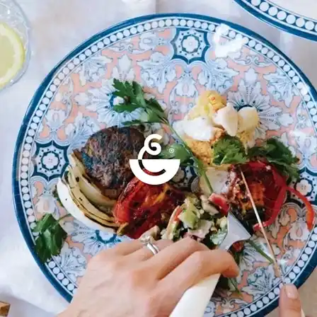 Hand holding fork over colorful plated meal.
