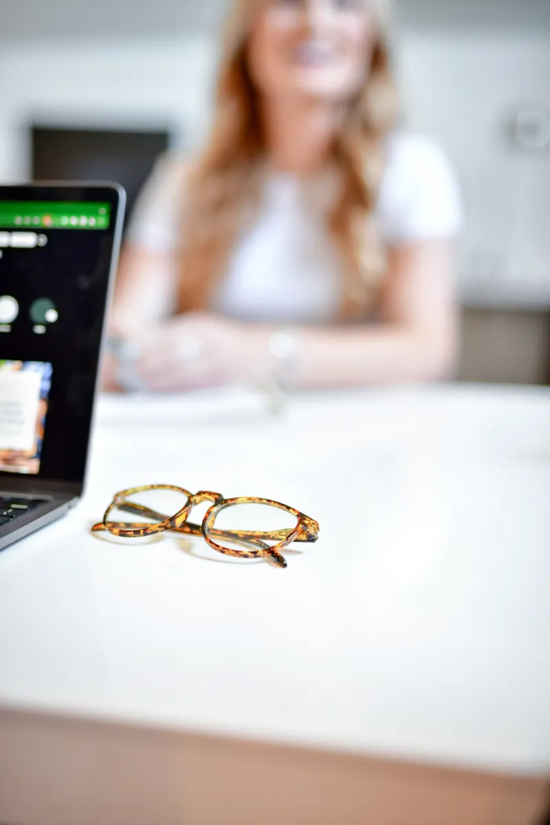 A pair of glasses sits folded on a white conference table.